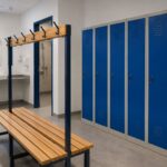 Vestuarios para centro deportivo: guía y equipamiento Vestuario de centro deportivo con taquillas metálicas azules, banco central de madera, lavabos y zona de ducha